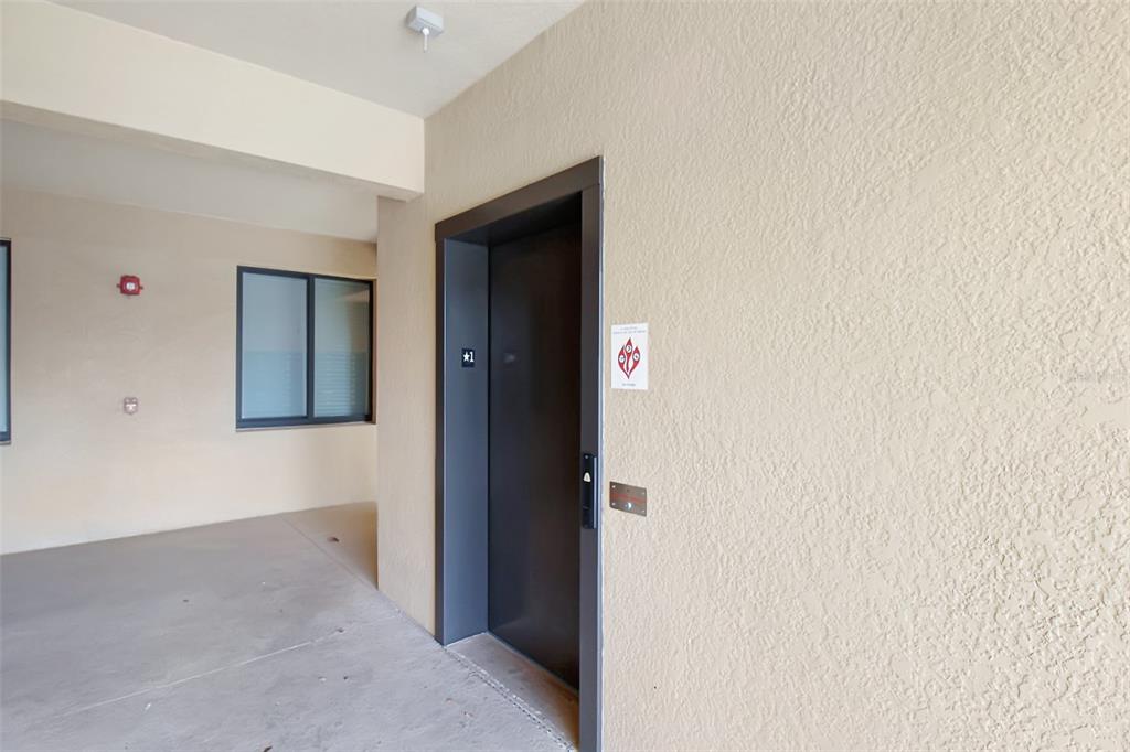 A dark elevator door is set into a beige stucco wall in an outdoor hallway — 6519 GRAND ESTUARY TRAIL UNIT 302, BRADENTON, FL