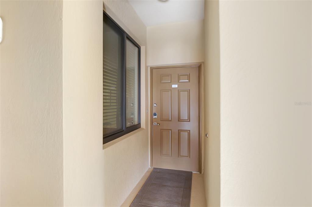 A tan exterior entryway features a brown door with a window and a floor mat — 6519 GRAND ESTUARY TRAIL UNIT 302, BRADENTON, FL
