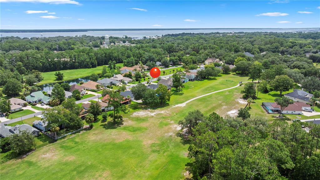 An aerial view shows a residential neighborhood with houses bordering a large, open grassy field — 3729 CONSTANCIA DRIVE, GREEN COVE SPRINGS, FL