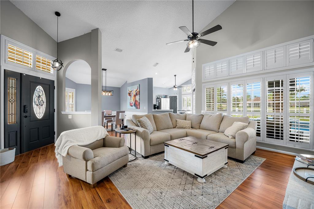 A living room features a sectional sofa, an armchair, wood flooring, and plantation shutters — 3729 CONSTANCIA DRIVE, GREEN COVE SPRINGS, FL