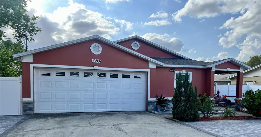 A red, single-story house features a two-car garage, stone accents, and a paved driveway — 10804 N MYRTLE STREET, TAMPA, FL