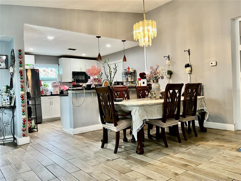 A dining area with a chandelier and table sits adjacent to an open-concept white kitchen — 10804 N MYRTLE STREET, TAMPA, FL