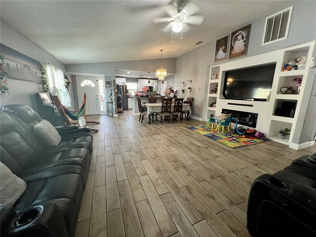 A living room with wood-look tile flooring, a large television unit, and an adjacent dining area — 10804 N MYRTLE STREET, TAMPA, FL