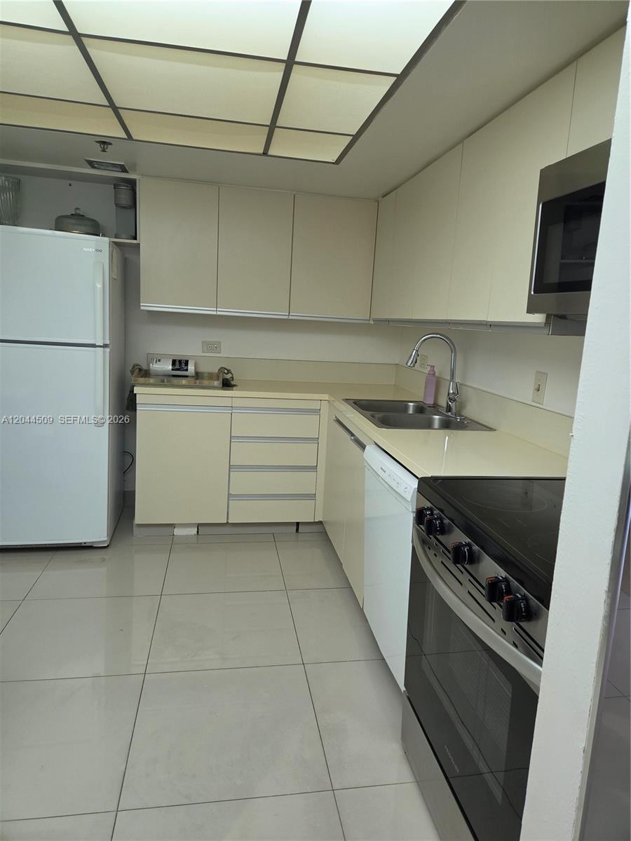 A kitchen features white cabinets, light countertops, a white refrigerator, and a stainless steel stove — HOLLYWOOD, FL