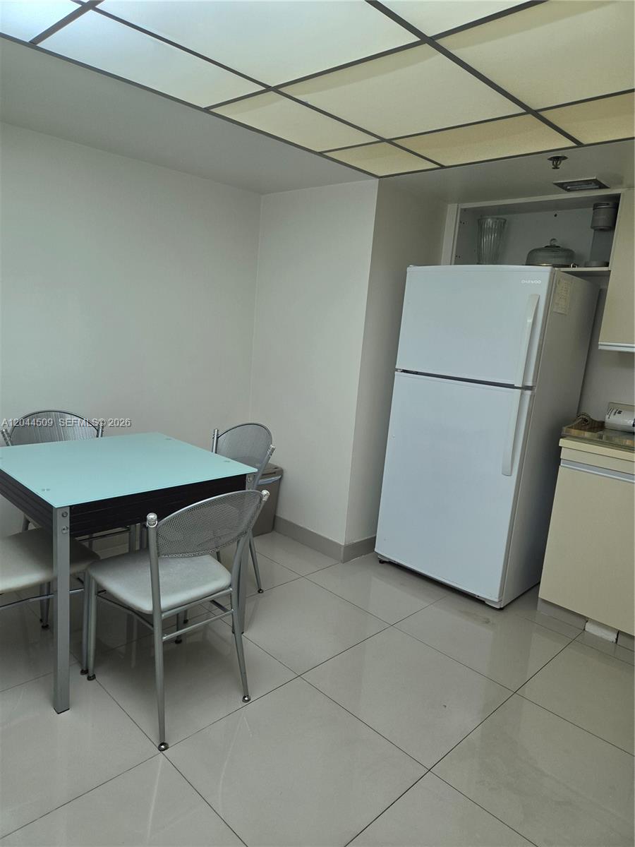 A dining area features a glass-topped table, metal chairs, and a white refrigerator on tile flooring — HOLLYWOOD, FL