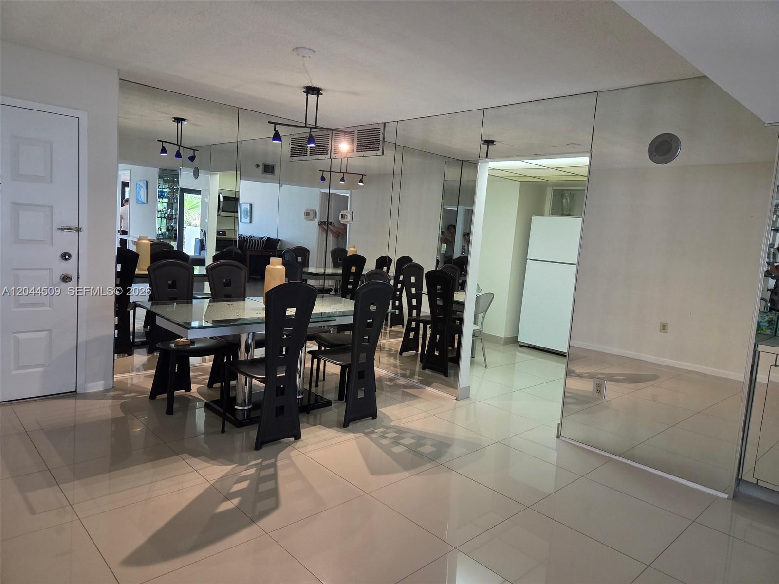 A dining room features a glass-topped table, black chairs, and mirrored walls on tile flooring — HOLLYWOOD, FL