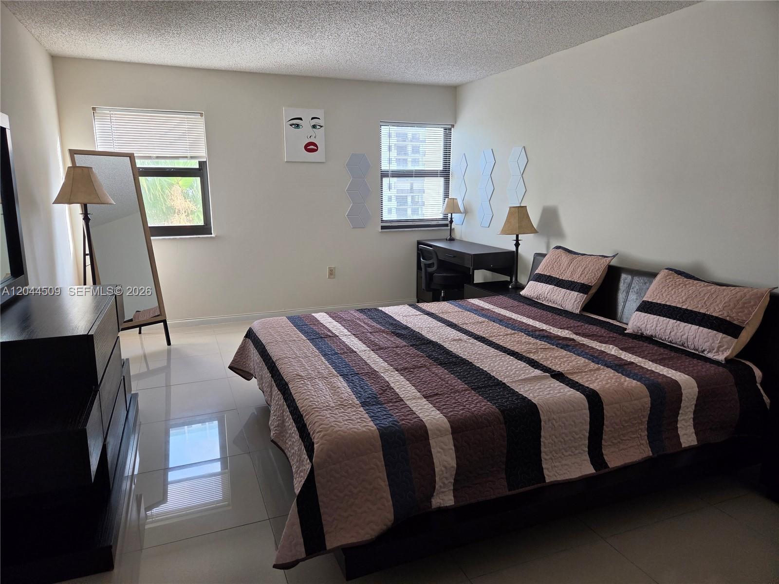 A bedroom features a striped bedspread, tiled floors, a desk, and a full-length mirror — HOLLYWOOD, FL