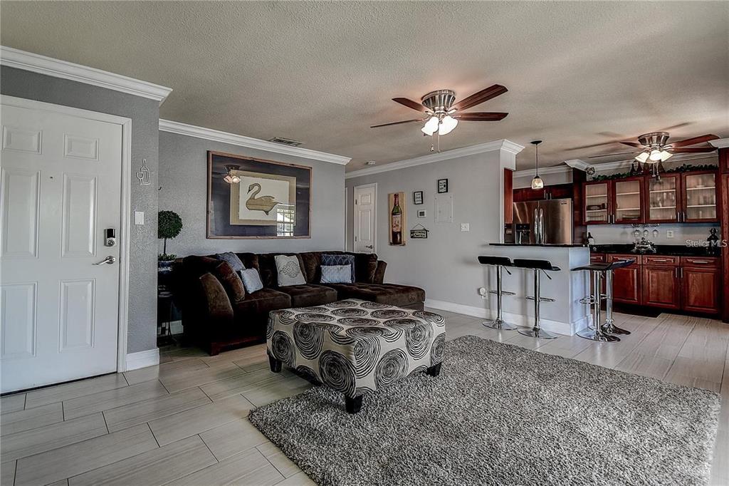 A living room with a brown sectional sofa, patterned ottoman, and an open kitchen area — 5111 COQUINA KEY DRIVE SE UNIT C, ST PETERSBURG, FL