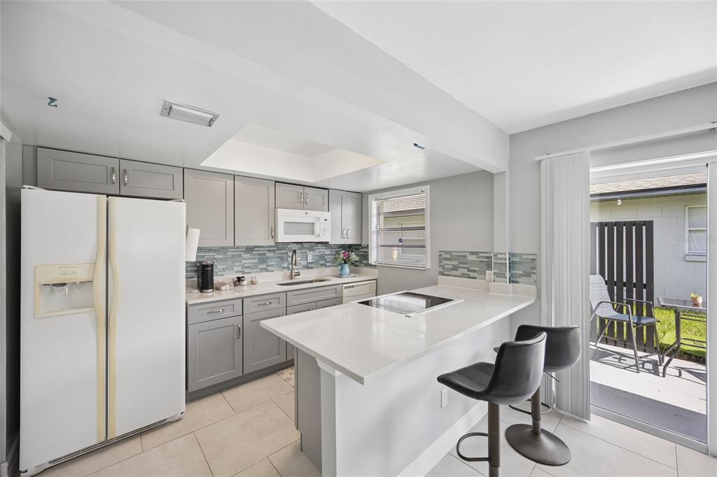 A kitchen with gray cabinets, white countertops, a breakfast bar, and a sliding glass door — 536 HIBISCUS WAY UNIT 7B, ORLANDO, FL