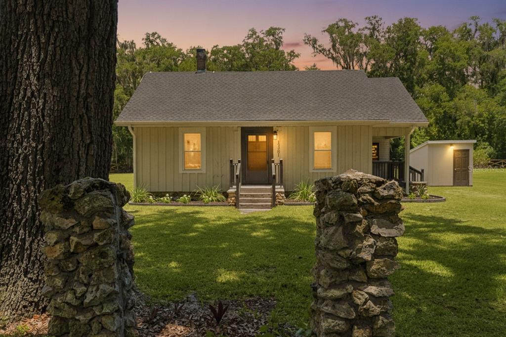 A light-colored cottage with a dark roof sits behind two stone pillars on a lawn — 13281 SE 122ND PLACE, OCKLAWAHA, FL