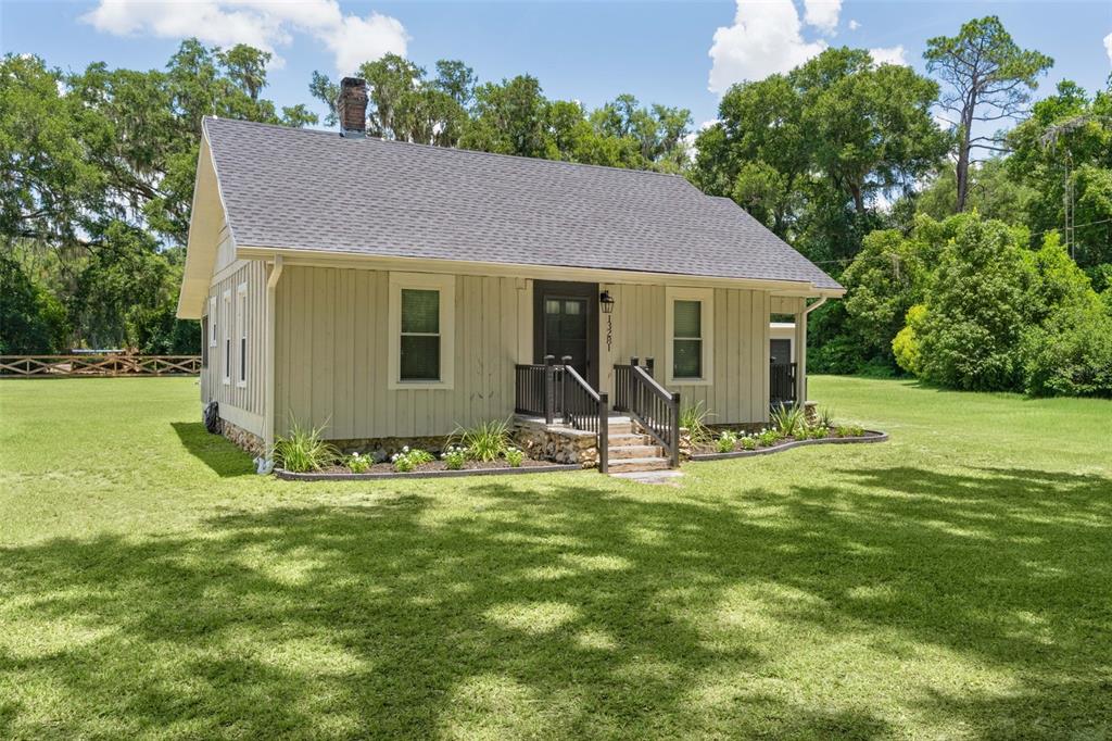 A single-story house with board-and-batten siding sits on a large, grassy lawn with trees — 13281 SE 122ND PLACE, OCKLAWAHA, FL