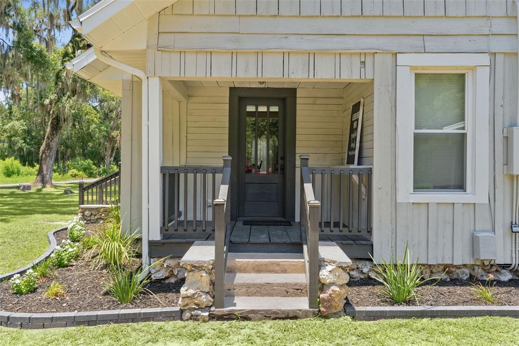 A front porch with a dark door, wooden railing, and stone steps leading to the entrance — 13281 SE 122ND PLACE, OCKLAWAHA, FL