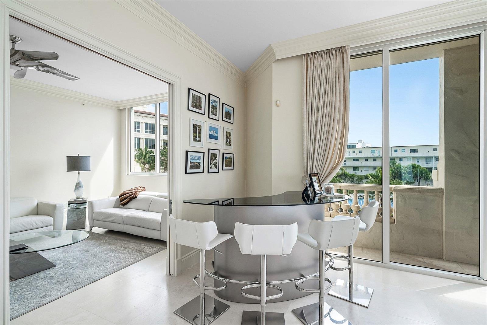 A modern bar area with white stools sits next to a living room and balcony — 3000 S Ocean Boulevard # 402, Palm Beach FL 33480, PALM BEACH, FL
