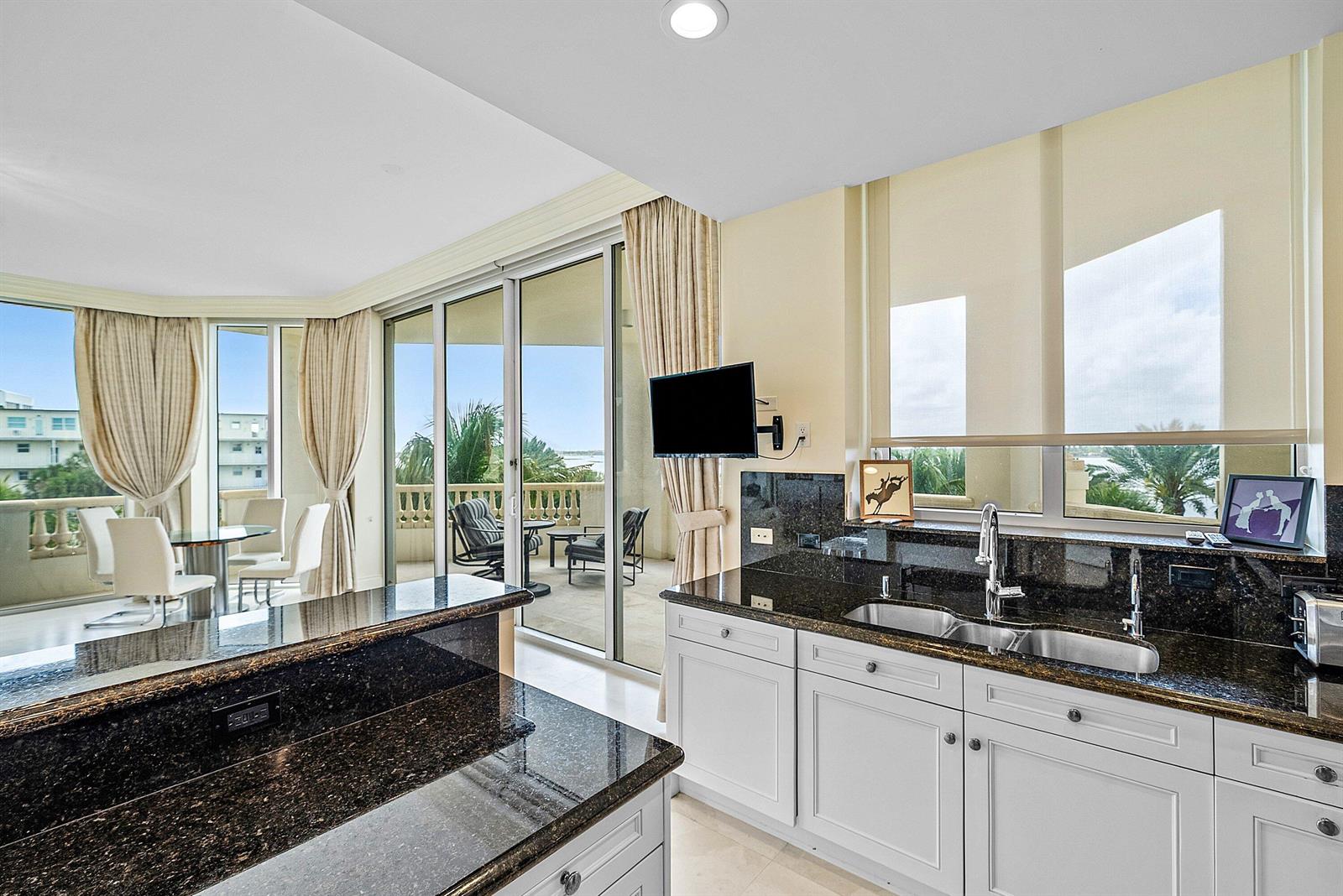 A kitchen with dark granite countertops and white cabinets overlooks a balcony with water views — 3000 S Ocean Boulevard # 402, Palm Beach FL 33480, PALM BEACH, FL