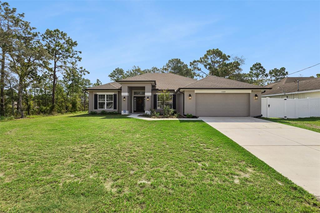 A single-story suburban house with a tan exterior, a two-car garage, and a grassy lawn — 11268 KODIAK WREN ROAD, WEEKI WACHEE, FL