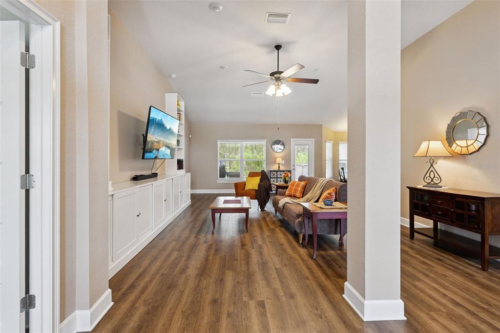 A living room features wood-look flooring, a ceiling fan, built-in cabinetry, and a mounted television — 11268 KODIAK WREN ROAD, WEEKI WACHEE, FL