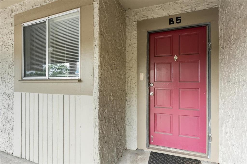 A red front door labeled B5 sits next to a window with blinds on a stucco wall — 6332 NEWTOWN CIRCLE UNIT 32B5, TAMPA, FL