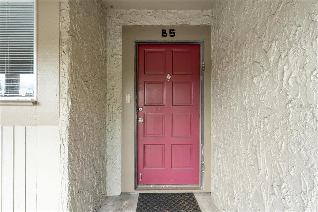 A red front door labeled B5 is set into a textured beige exterior wall — 6332 NEWTOWN CIRCLE UNIT 32B5, TAMPA, FL