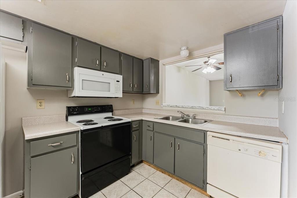 A kitchen features gray cabinets, white appliances, a double sink, and light-colored tile flooring — 6332 NEWTOWN CIRCLE UNIT 32B5, TAMPA, FL