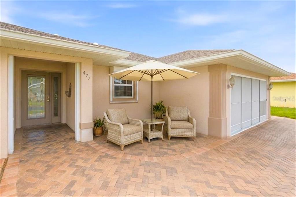 A paved patio features two wicker chairs, a small table, and an umbrella under a roof — 477 SWEETWATER WAY, HAINES CITY, FL