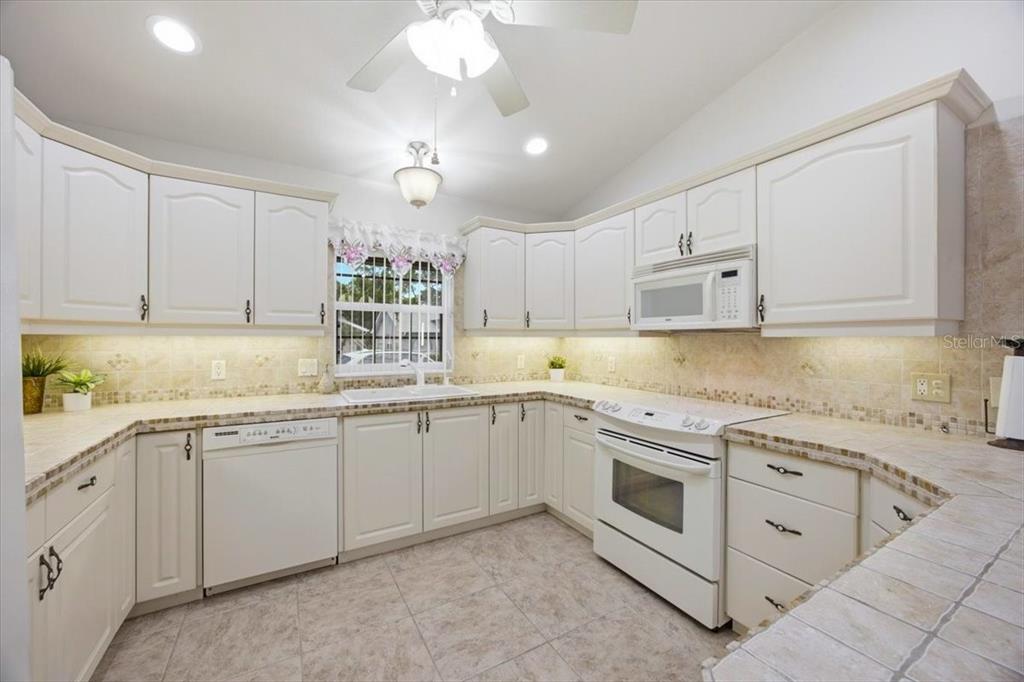 A kitchen with white cabinets, tile countertops, a white appliance suite, and tile flooring — 477 SWEETWATER WAY, HAINES CITY, FL