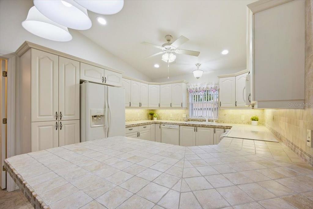 A kitchen features white cabinets, a tiled countertop, and a ceiling fan — 477 SWEETWATER WAY, HAINES CITY, FL