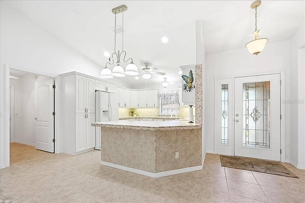 A kitchen with white cabinets and a tiled island sits next to a front entryway — 477 SWEETWATER WAY, HAINES CITY, FL