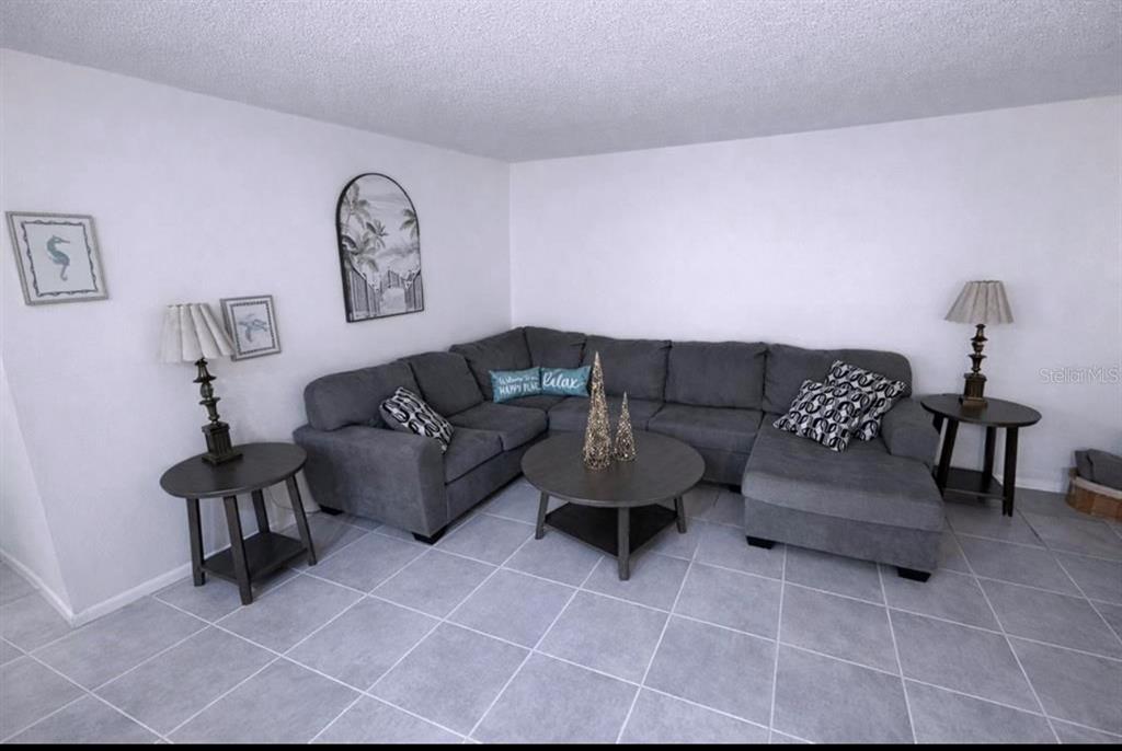 A living room features a gray sectional sofa, a round coffee table, and tile flooring — 3300 FOX CHASE CIRCLE N UNIT 229, PALM HARBOR, FL
