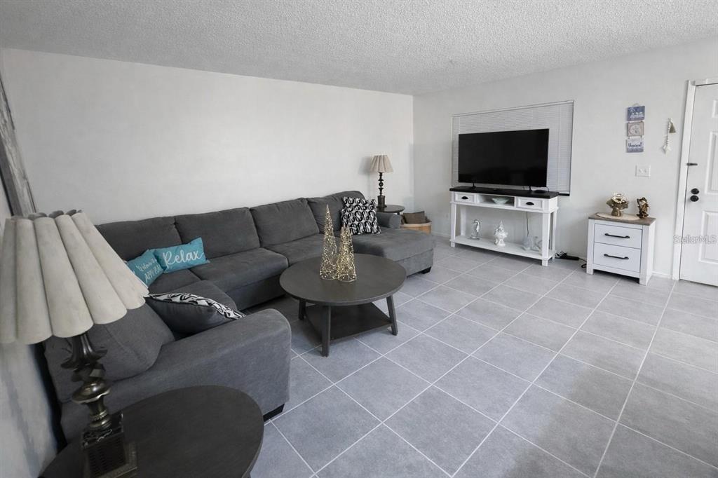 A living room features a gray sectional sofa, a round coffee table, and tile flooring — 3300 FOX CHASE CIRCLE N UNIT 229, PALM HARBOR, FL