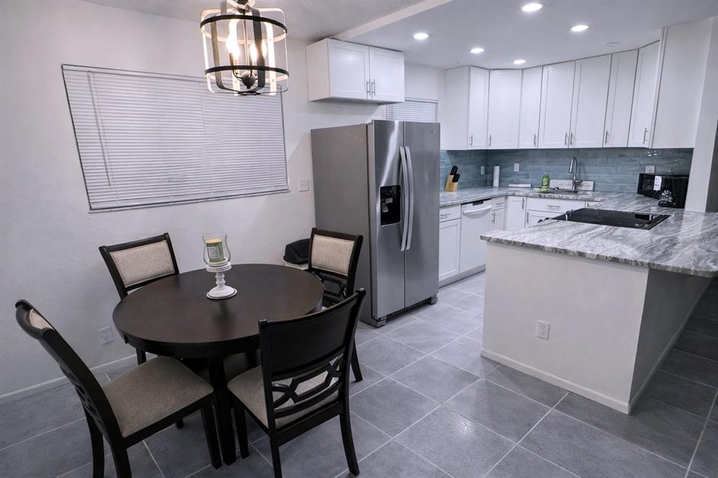 A dining area with a round table and a kitchen featuring white cabinets and gray countertops — 3300 FOX CHASE CIRCLE N UNIT 229, PALM HARBOR, FL