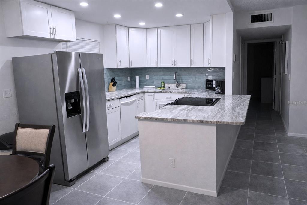 A kitchen features white cabinets, stainless steel appliances, and a gray stone countertop island — 3300 FOX CHASE CIRCLE N UNIT 229, PALM HARBOR, FL