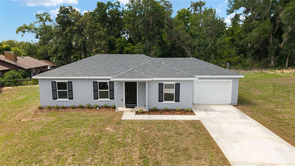 A single-story gray house with a black front door, dark shutters, and a concrete driveway — 3 JUNIPER PASS PLACE, OCALA, FL