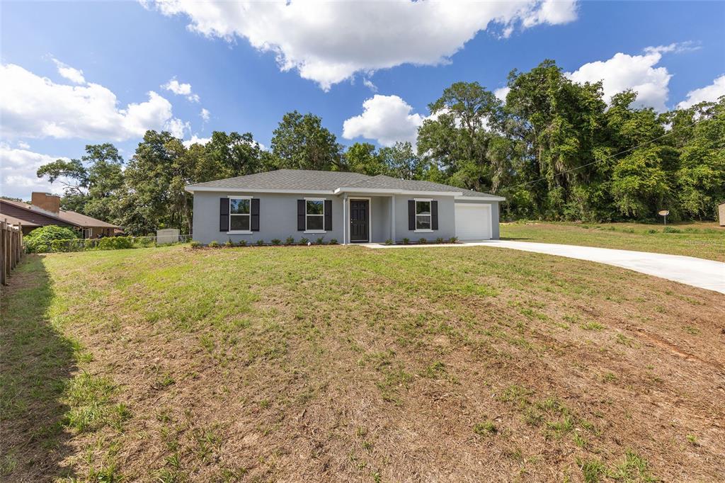 A single-story gray house with a white garage and a large, sparse front lawn — 3 JUNIPER PASS PLACE, OCALA, FL