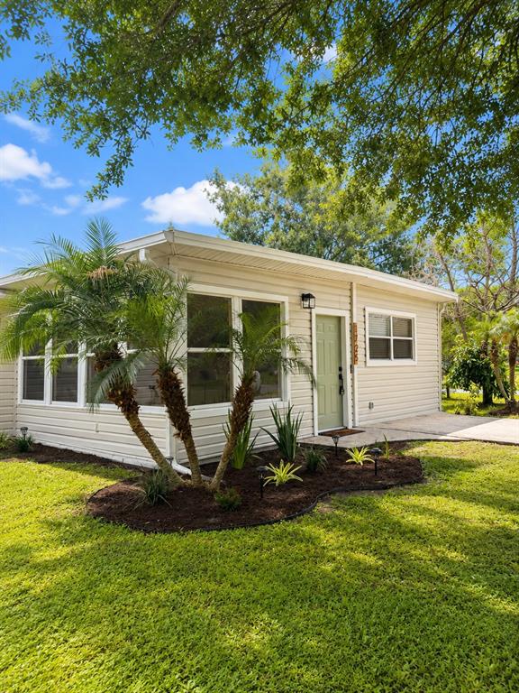 A light-colored, single-story house exterior features a palm tree, a green door, and landscaping — 1725 PARK DRIVE, LAKELAND, FL