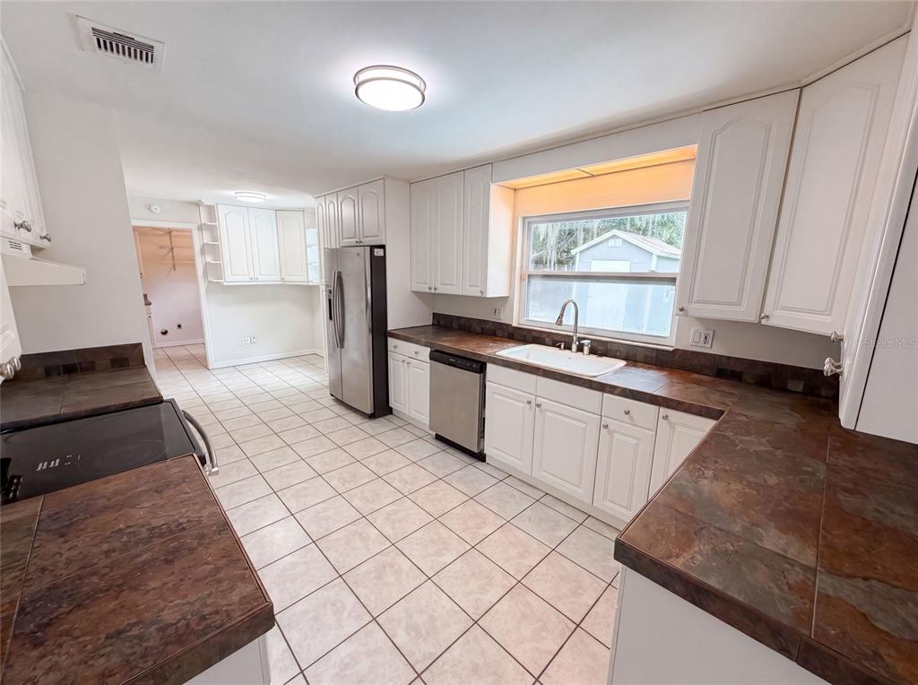 A kitchen features white cabinets, dark tile countertops, stainless steel appliances, and light floor tiles — 963 SEQUOIA DRIVE, WINTER SPRINGS, FL