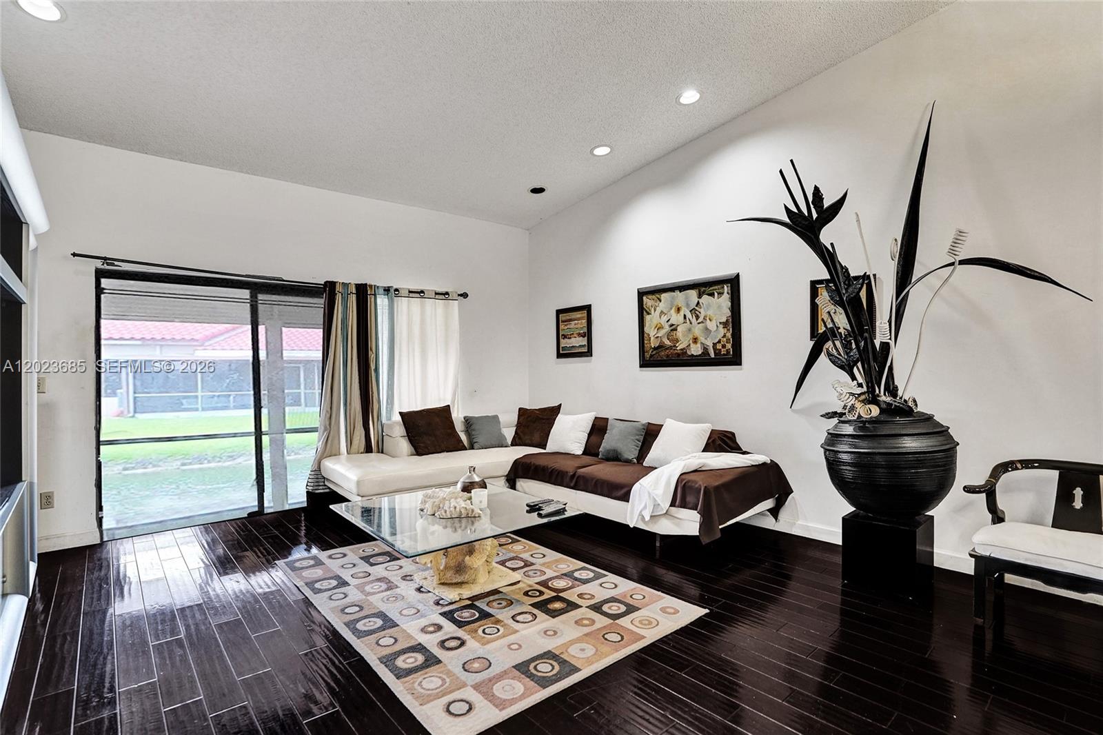 A living room features dark wood floors, a sectional sofa, and a large decorative plant — 3273 W Inverrary Blvd W, Lauderhill FL 33319, LAUDERHILL, FL