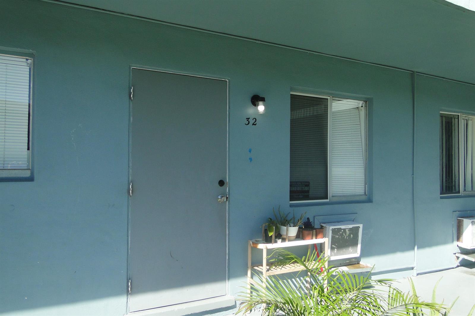 A blue exterior wall features a door numbered 32, a window, and a small plant stand — 1829 N A Street # 32, FL 33460, FL