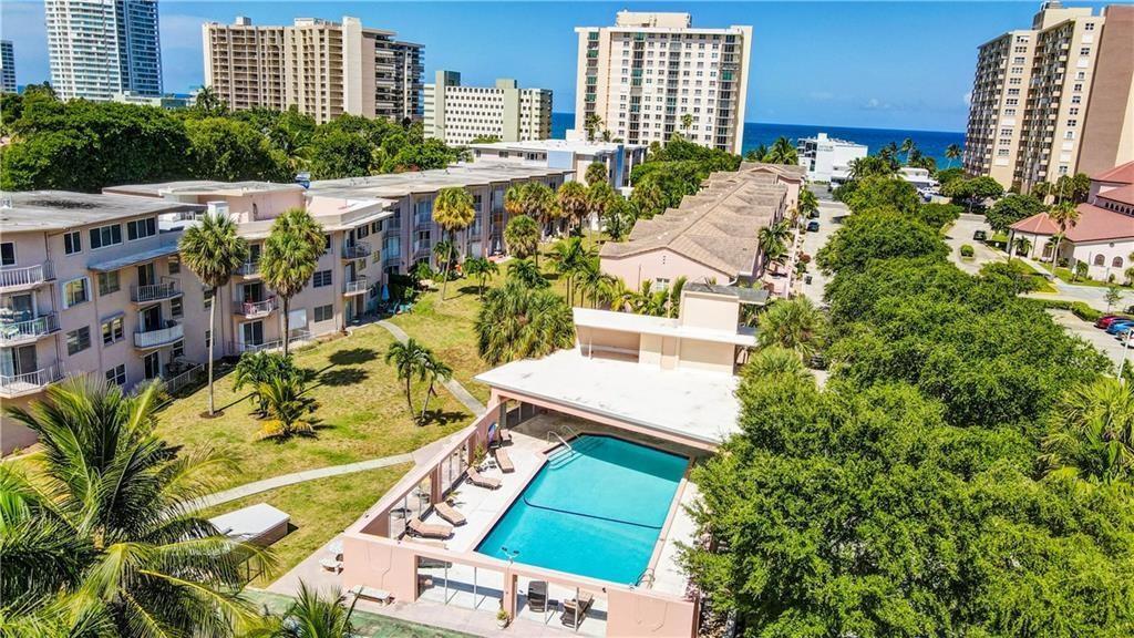 An aerial view shows a swimming pool area surrounded by apartment buildings and lush trees — 1967 S Ocean Boulevard # D, Pompano Beach FL 33062, POMPANO BEACH, FL