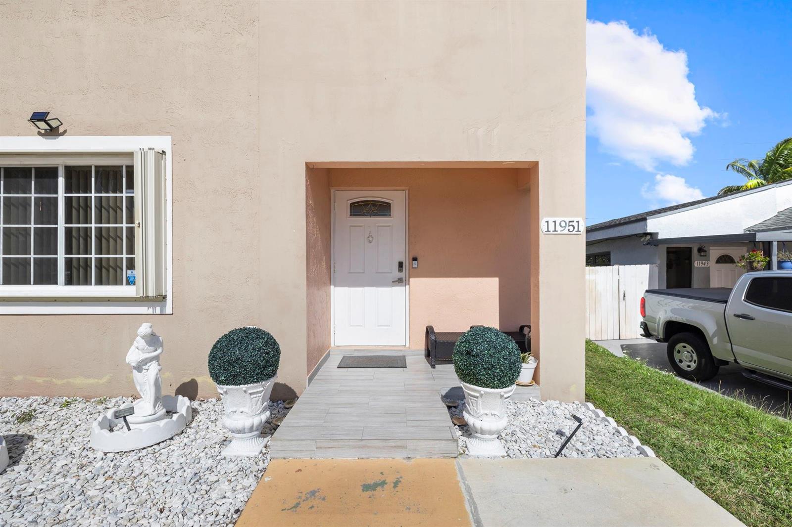The exterior of a peach-colored house features a white front door and two decorative planters — 11951 SW 208th Terrace, Miami FL 33177, MIAMI, FL
