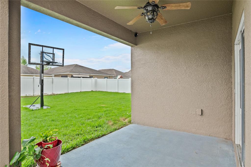 A covered concrete patio overlooks a grassy backyard with a basketball hoop and white fence — 13161 ROYAL PINES AVENUE, RIVERVIEW, FL