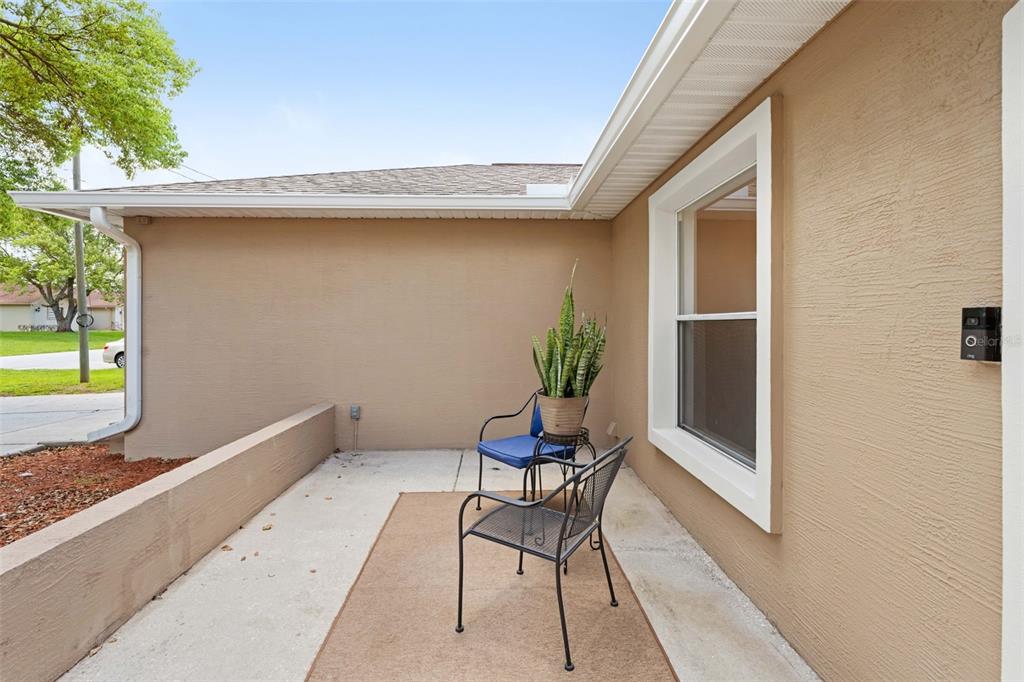 A concrete patio features two metal chairs, a potted plant, and a beige exterior wall — 11487 KERRIDALE AVENUE, SPRING HILL, FL