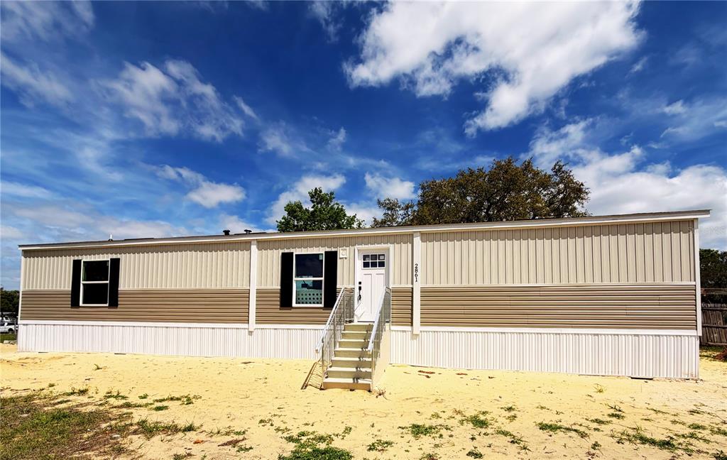 A single-story manufactured home with beige and brown siding sits on a sandy lot — 2861 FAST TROT TRAIL, LAKE WALES, FL