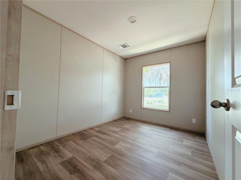 An empty room features light-colored walls, wood-look flooring, a single window, and a ceiling light — 2861 FAST TROT TRAIL, LAKE WALES, FL