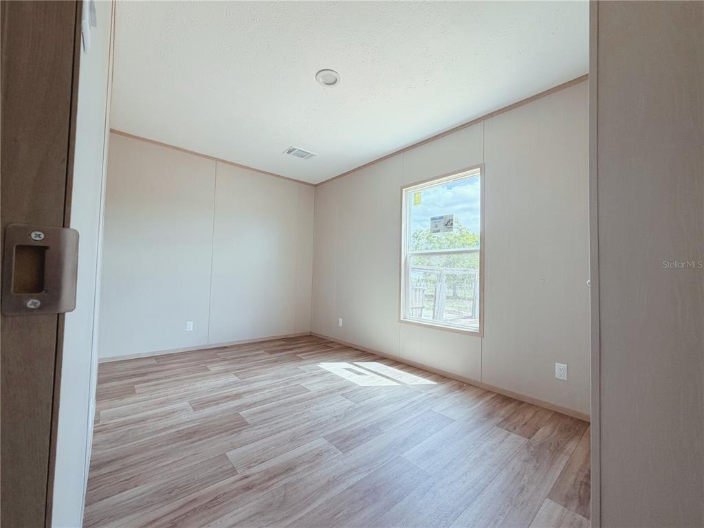 An empty bedroom features light-colored walls, wood-look vinyl flooring, and a single window — 2861 FAST TROT TRAIL, LAKE WALES, FL