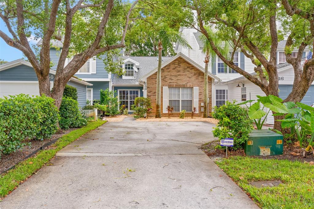 A concrete driveway leads to a brick and blue-sided house with mature trees and landscaping — 248 ST IVES DRIVE UNIT 248, PALM HARBOR, FL