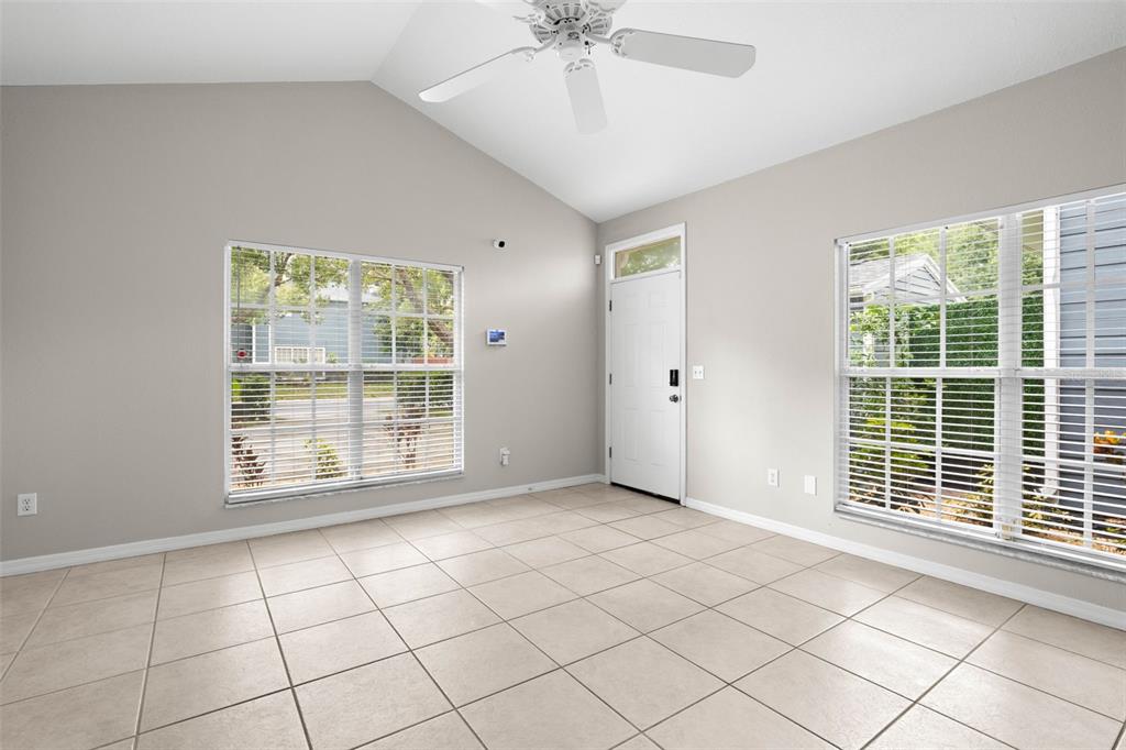 An empty room with light-colored tile floors, vaulted ceilings, a ceiling fan, and two windows — 248 ST IVES DRIVE UNIT 248, PALM HARBOR, FL
