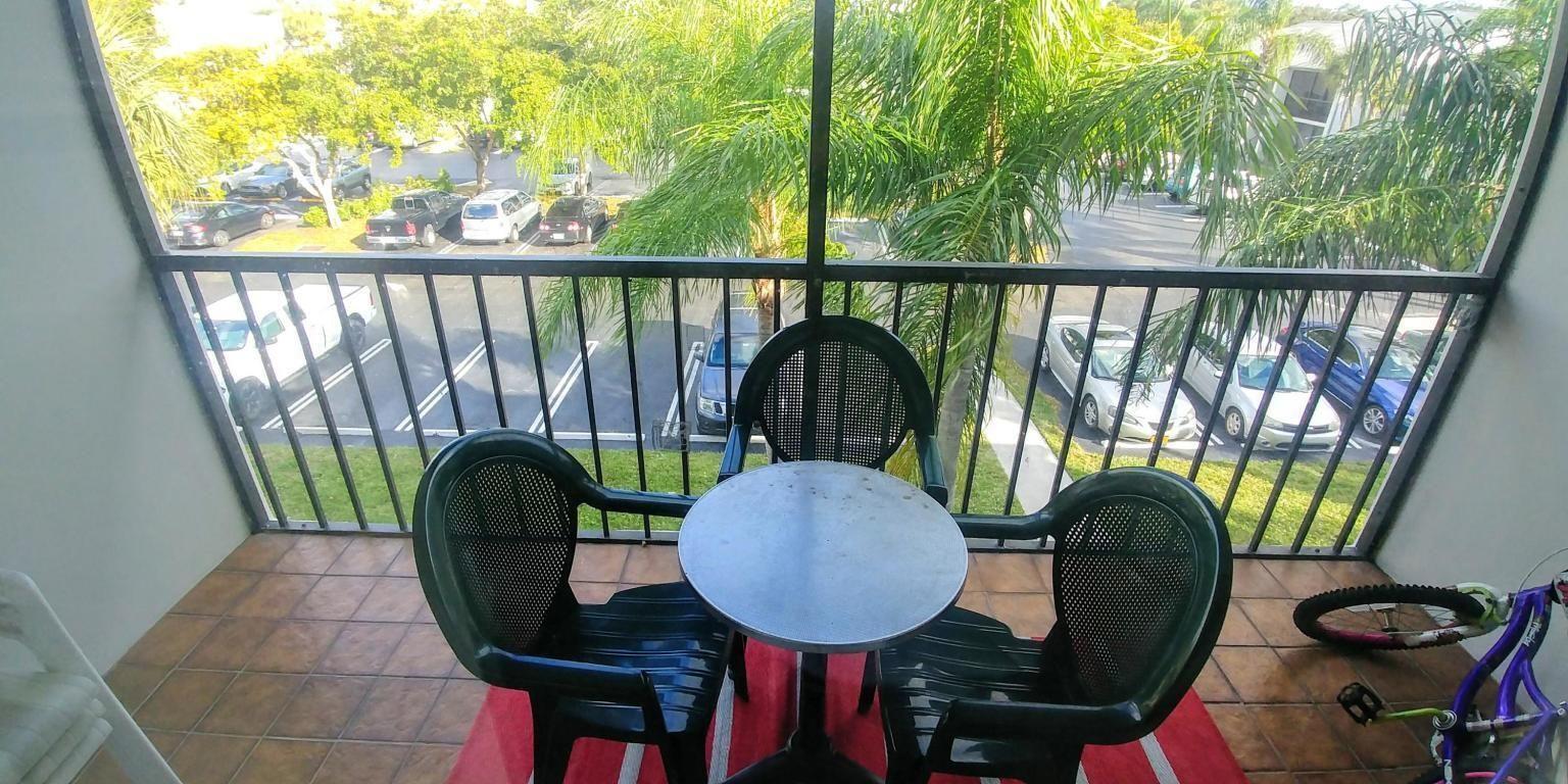 A balcony with a small table, two chairs, and a view of a parking lot — 1009 Green Pine Boulevard # D3, West Palm Beach FL 33409, WEST PALM BEACH, FL