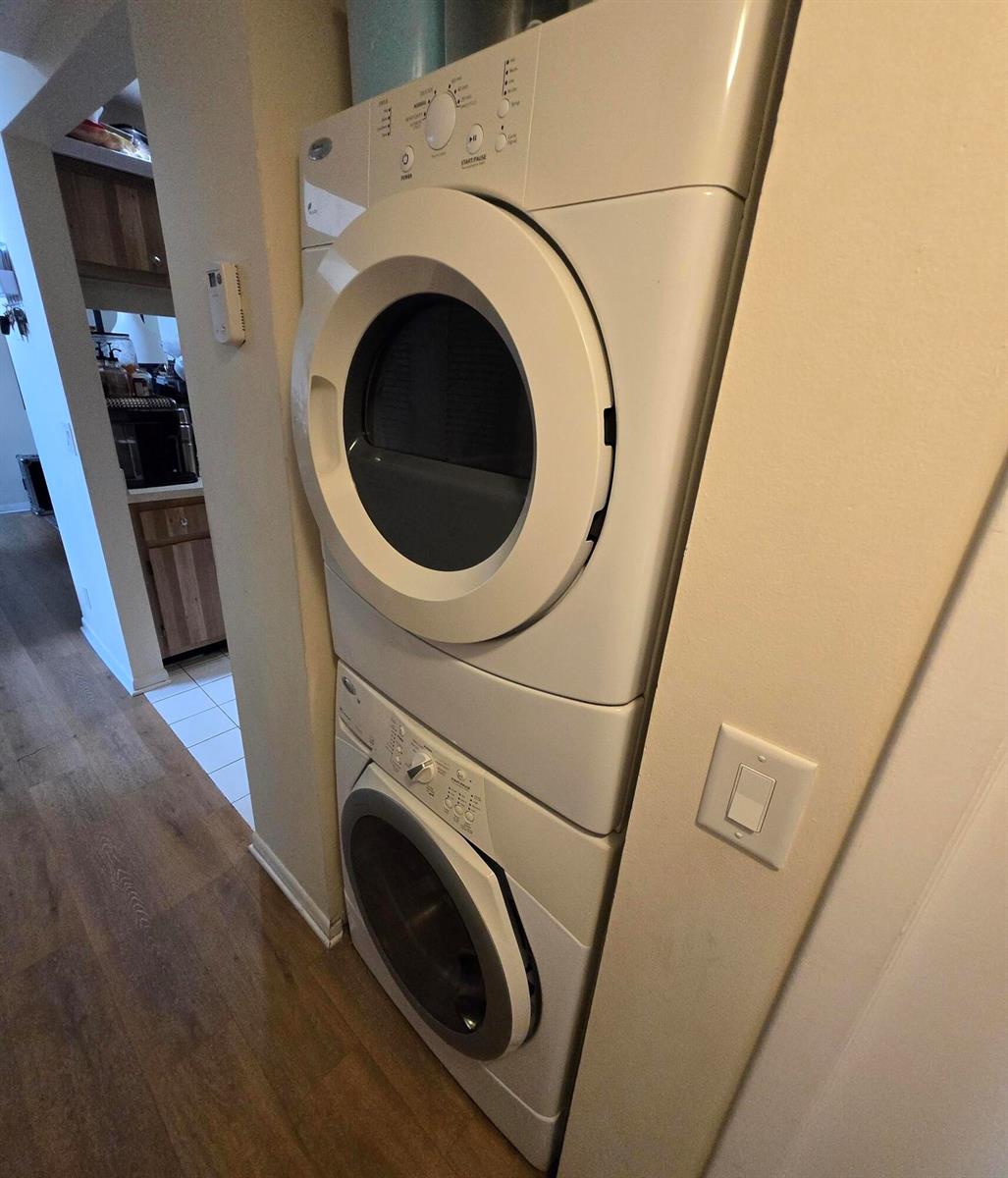 A stacked white washer and dryer unit is positioned in a hallway near a kitchen — 1009 Green Pine Boulevard # D3, West Palm Beach FL 33409, WEST PALM BEACH, FL