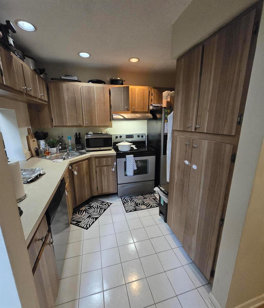 A kitchen features wood cabinets, stainless steel appliances, white tile flooring, and recessed lighting — 1009 Green Pine Boulevard # D3, West Palm Beach FL 33409, WEST PALM BEACH, FL