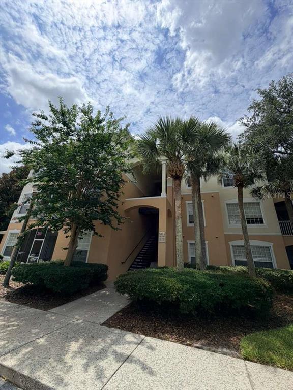 A three-story tan apartment building with palm trees and a sidewalk in the foreground — 6214 STEVENSON DRIVE UNIT 303, ORLANDO, FL